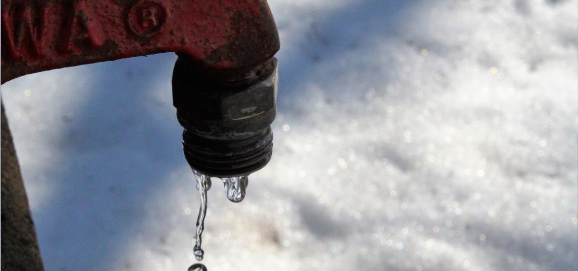 Red tap leaking water onto snow