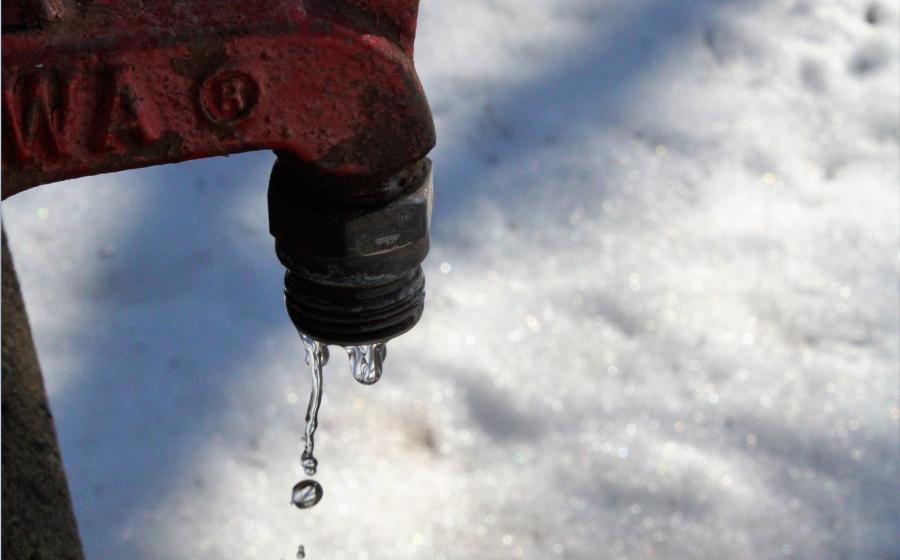 Red tap leaking water onto snow