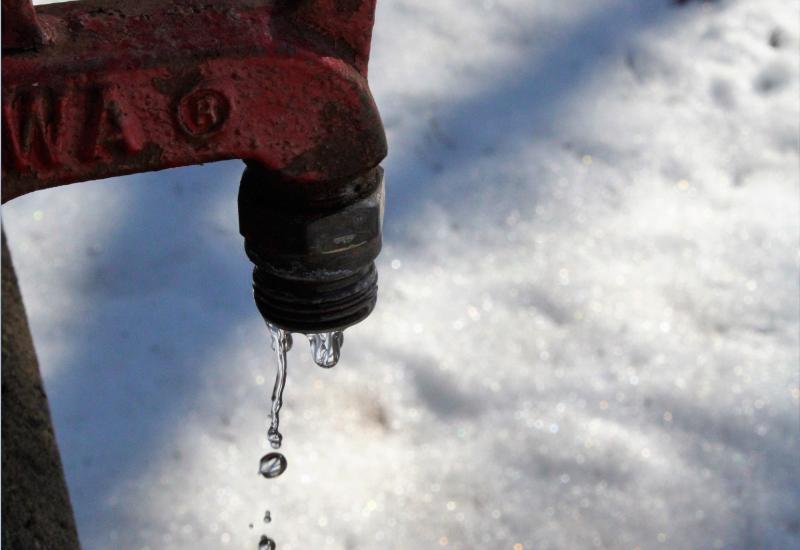 Red tap leaking water onto snow